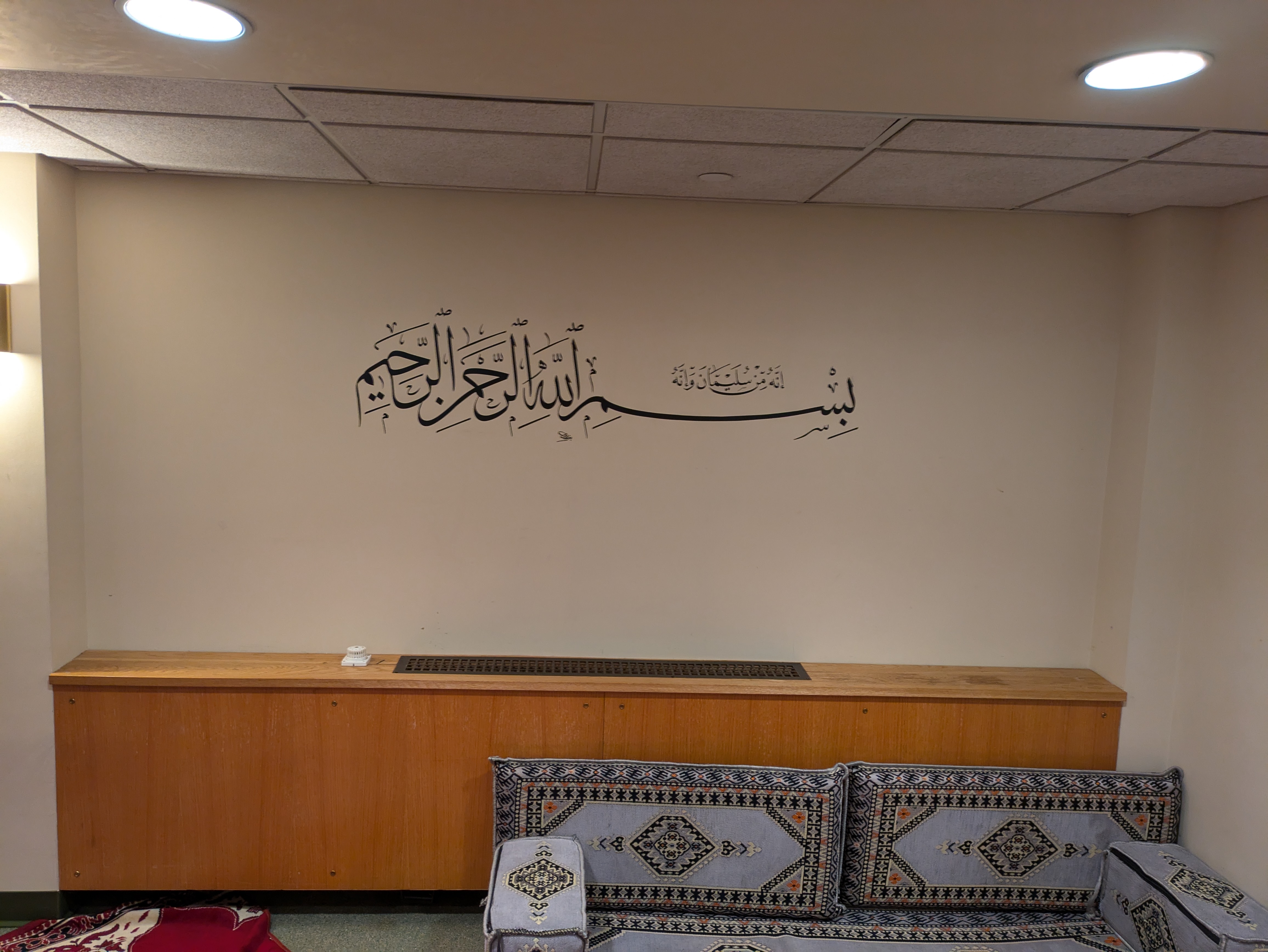 The Musalla at Yale, with a low couch underneath a wall with arabic script.