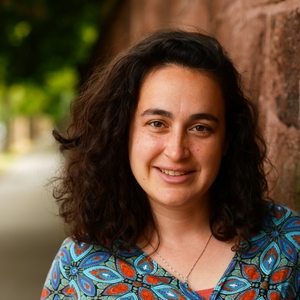 Maytal Saltiel, a light skinned woman with shoulder length curly dark brown hair, smiling towards the camera.