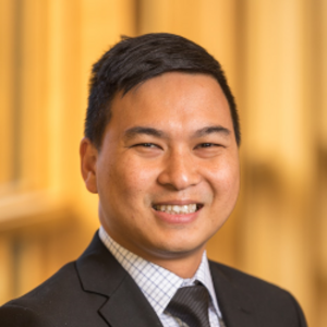 Allan Esteron, an asian man with short black hair wearing a suit, smiling against a blurred yellow background