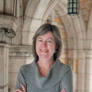 Sharon Kugler, a white woman with shoulder length grey hair, smiling in front of collegiate gothic architecture