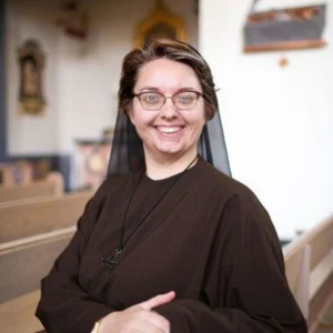 Sister Mary Rose Irvine, a white woman with short brown hair and glasses, wearing a wimple and habit, inside a church