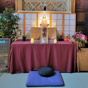 An altar draped in a red cloth with a statue of the Buddha and lit candles on it.