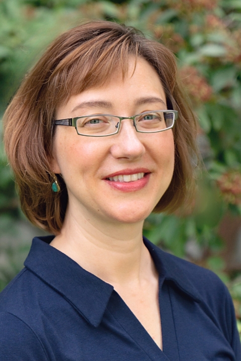 Sumi Kim, a white woman with square glasses and a bob of auburn hair, smiling at the camera