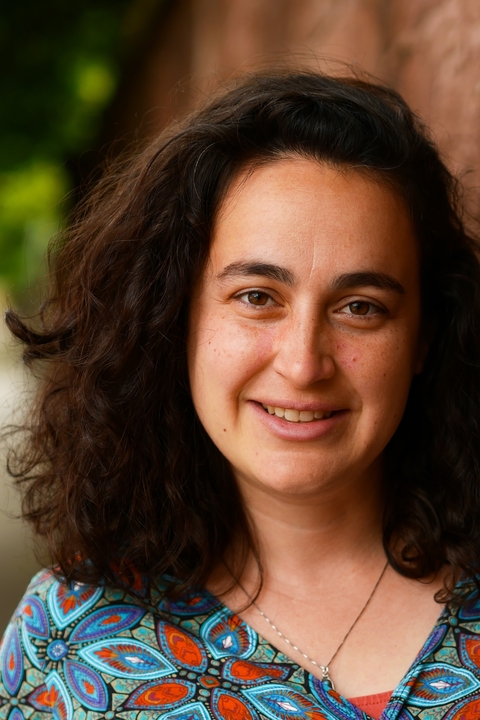 Maytal Saltiel, a light skinned woman with shoulder length curly dark brown hair, smiling towards the camera.