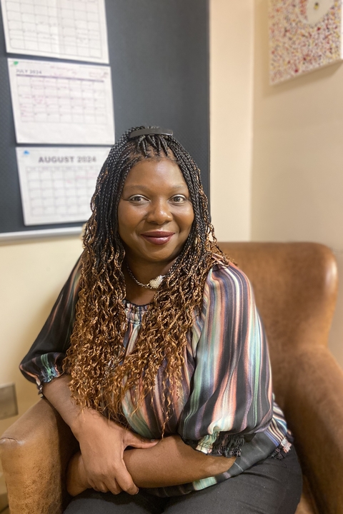 A photo of Tammie McKenzie, a Black woman with ombre'd hair in long braids, sitting in an armchair