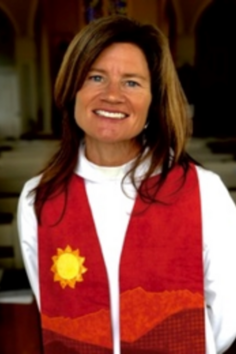 alison donohue, a white woman with shoulder length dark hair and blonde highlights, wearing a white cassock and red stole