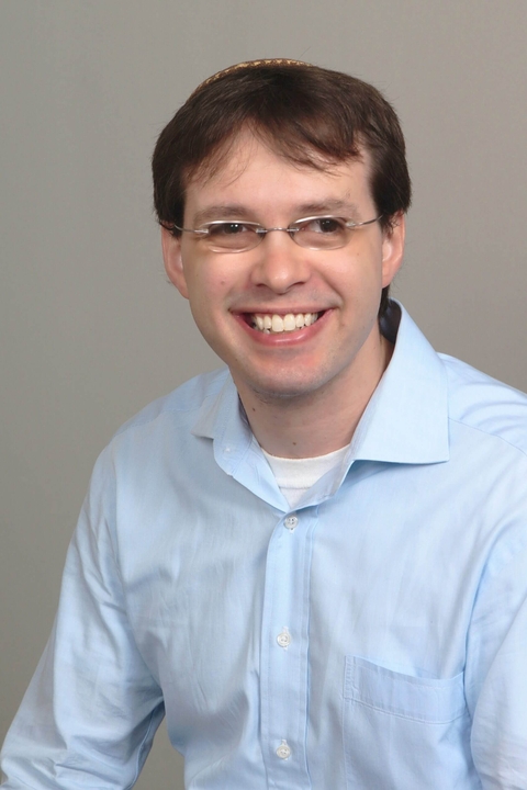 Alex Ozar, a white man with short brown hair wearing glasses and a yarmulke, smiling to the camera