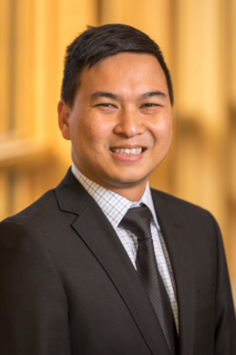 Allan Esteron, an asian man with short black hair wearing a suit, smiling against a blurred yellow background