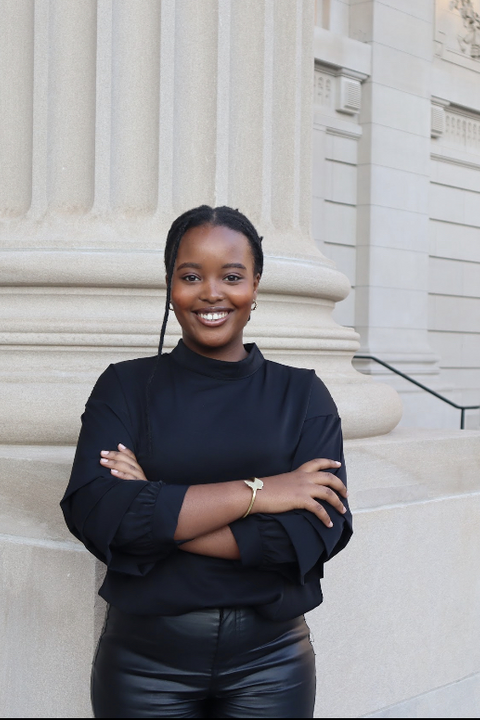 Audrey Gatera, a black woman with her hair in a braid, smiling towards the camera in front of fluted columns.