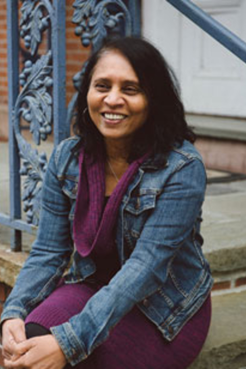 Chitra, a south asian woman with shoulder length dark hair, smiling and sitting on a stoop
