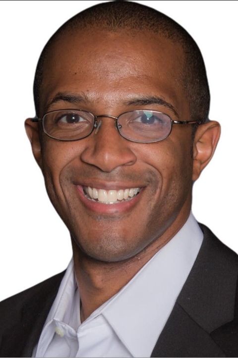 OrLando Yarborough, a black man with very short cropped hair wearing glasses and a suit, smiling in front of a white background.