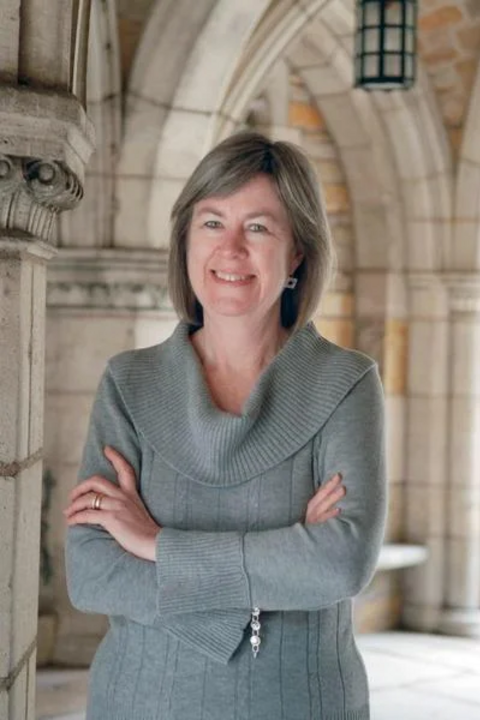 Sharon Kugler, a white woman with shoulder length grey hair, smiling in front of collegiate gothic architecture