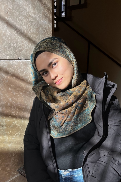 Ishnan Khan, a light skinned woman wearing a patterned hijab, smiling towards the camera.