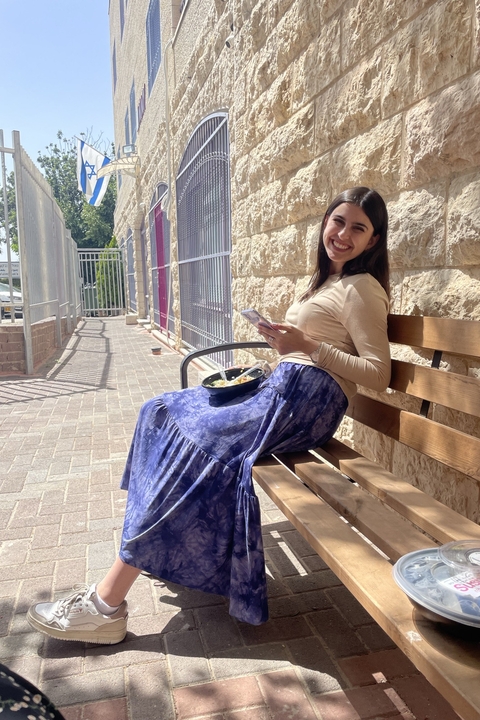 Sabrina Zbar, a white woman with long dark brown hair, leaning back on a bench in the sun.