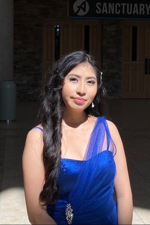 Wendy Cruz, an asian woman with black hair in a long braid, wearing a blue dress standing against a dark backdrop