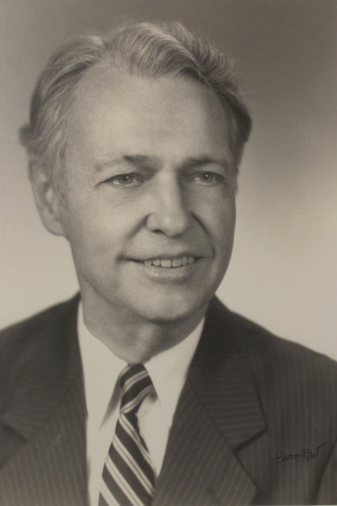 Harry Adams, a white man with short curly hair wearing a suit, in a black and white posed photographic portrait.