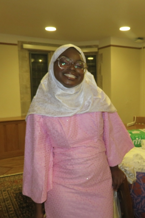 Haerat Alabi, a dark skinned hijabi woman wearing large glasses, smiling widely.