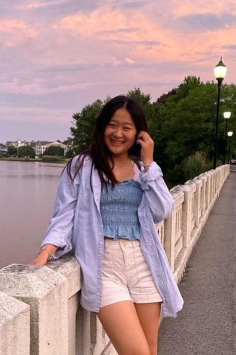 Michelle Mao, an Asian Woman with long black hair, smiling to camera in front of a sunset.