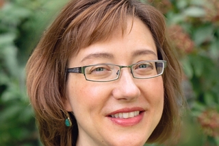 Sumi Kim, a white woman with square glasses and a bob of auburn hair, smiling at the camera