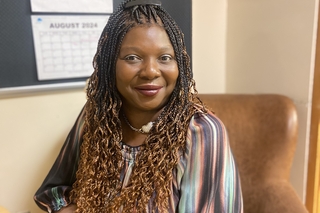 A photo of Tammie McKenzie, a Black woman with ombre'd hair in long braids, sitting in an armchair