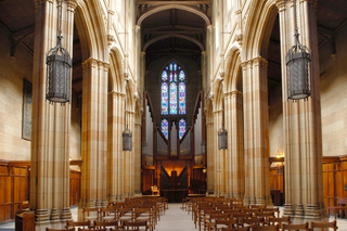 Wide shot of the pillars and arches of Dwight Chapel, with the stained glass lit by incoming sunlight.