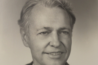 Harry Adams, a white man with short curly hair wearing a suit, in a black and white posed photographic portrait.