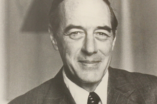 John Vannorsdall, a white man with short hair wearing a suit, smiling directly at the camera in a black and white photograph.