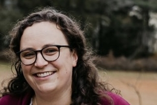 Jenny Peek, a white woman with curly brown hair wearing a red cardigan and black glasses.