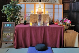 An altar draped in a red cloth with a statue of the Buddha and lit candles on it.