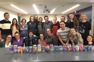 A group of students with multicolored jars in front of them on a long table.