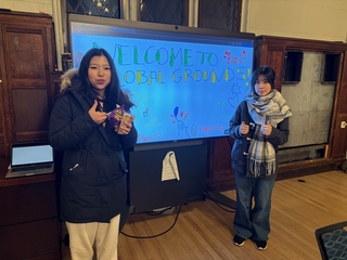 two people standing in front of a projected sign saying 'welcome to global grounds'.